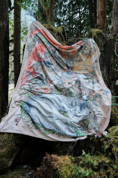 Fuzzy blanket featuring 5 sleeping foxes hanging on mossy stump