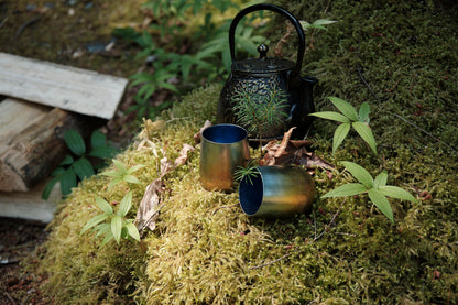 Two small titanium cups and a cast iron kettle sitting on a bed of moss