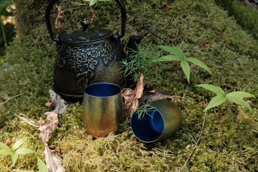 Two small titanium cups and a cast iron kettle sitting on a bed of moss