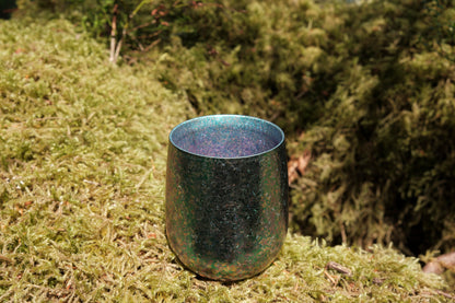 A large double wall titanium cup in the color crystal aquamarine sitting on a mossy stump