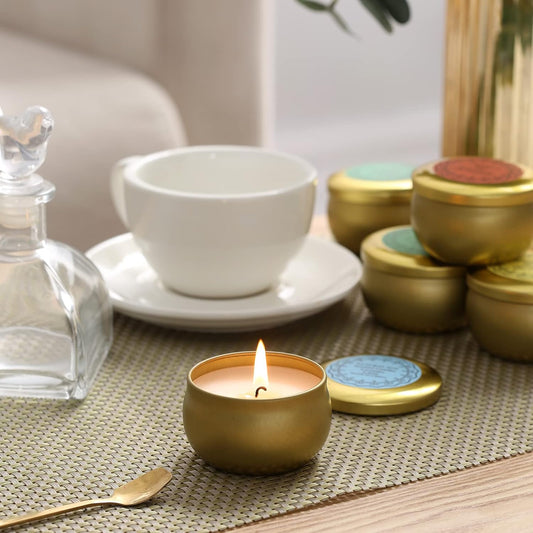 Burning candle in a gold round jar set on a table next to a cup of tea.