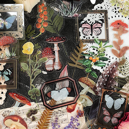 Stickers of mushrooms, ferns, butterflies, herbs, berries, feathers, and old picture frames spread across a table.