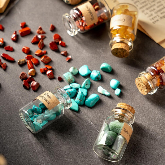 Several small jars filled with small gemstones spilled across the table. Each bottle has a label indicating what gem it contains.