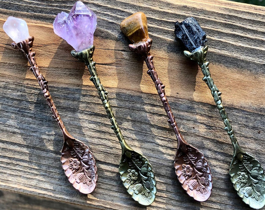 4 spoons that are a mix of copper and gold with various rough uncut gemstones at the end of the handle. The teaspoons feature embossing of garden like elements and leaves.